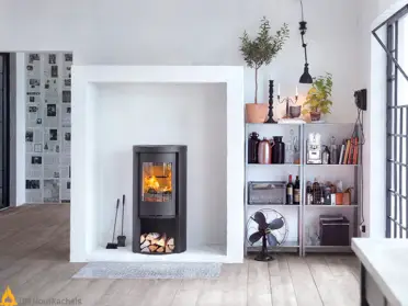 De Contura 520 Style houtkachel brandt in een lichte woonkamer met Scandinavisch design, zwarte gietijzeren deur, houtopslag en zicht op het vlammenspel.