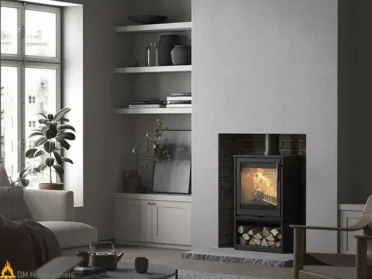 Een Contura 210 Style houtkachel brandt sfeervol in een strak interieur met ingebouwd houtvak en grote ruit voor zicht op het vuur.