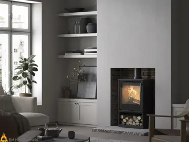 In een lichte woonkamer brandt de zwarte Contura 320TG houtkachel met spekstenen ombouw, terwijl houtblokken onder het vuurvak rustig liggen.