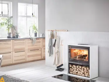 Tegen een strakke witte wand brandt de witte Contura 310G houtkachel met glazen deur, terwijl gespleten hout netjes is opgeborgen onderin.