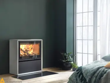 De Contura 320A vrijstaande houtkachel van Artstone verwarmt een moderne woonkamer met brede glazen deur en zicht op knisperend vuur bij het raam.