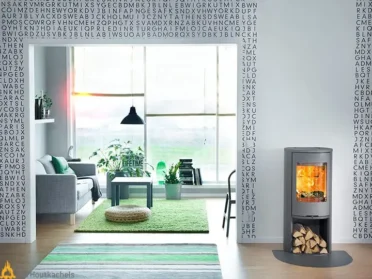 In een lichte woonkamer brandt de Contura 510 Style houtkachel in zwart en grijs, met zicht op het vlammenspel en een stapel hout eronder.