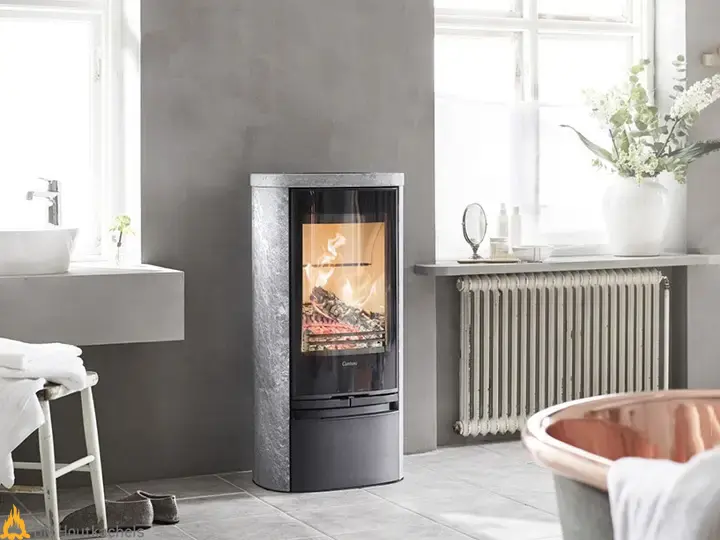 In een lichte badkamer brandt de grijze Contura 820TG Style houtkachel naast een radiator, met een rustige Scandinavische uitstraling.