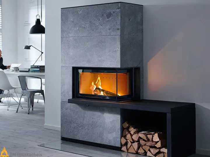 De Contura i41T in grijs speksteen brandt warm in een moderne woonkamer met open haardvak en gestapeld hout naast een lichte eethoek.
