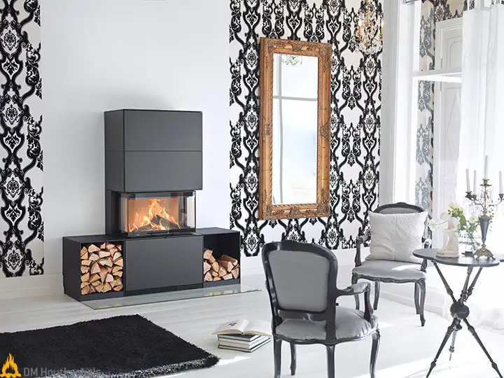 In een strak ingerichte woonkamer brandt de Contura i51 zwart staal met zicht op het vuur, naast opgestapeld haardhout en zwart-witte wandbekleding.