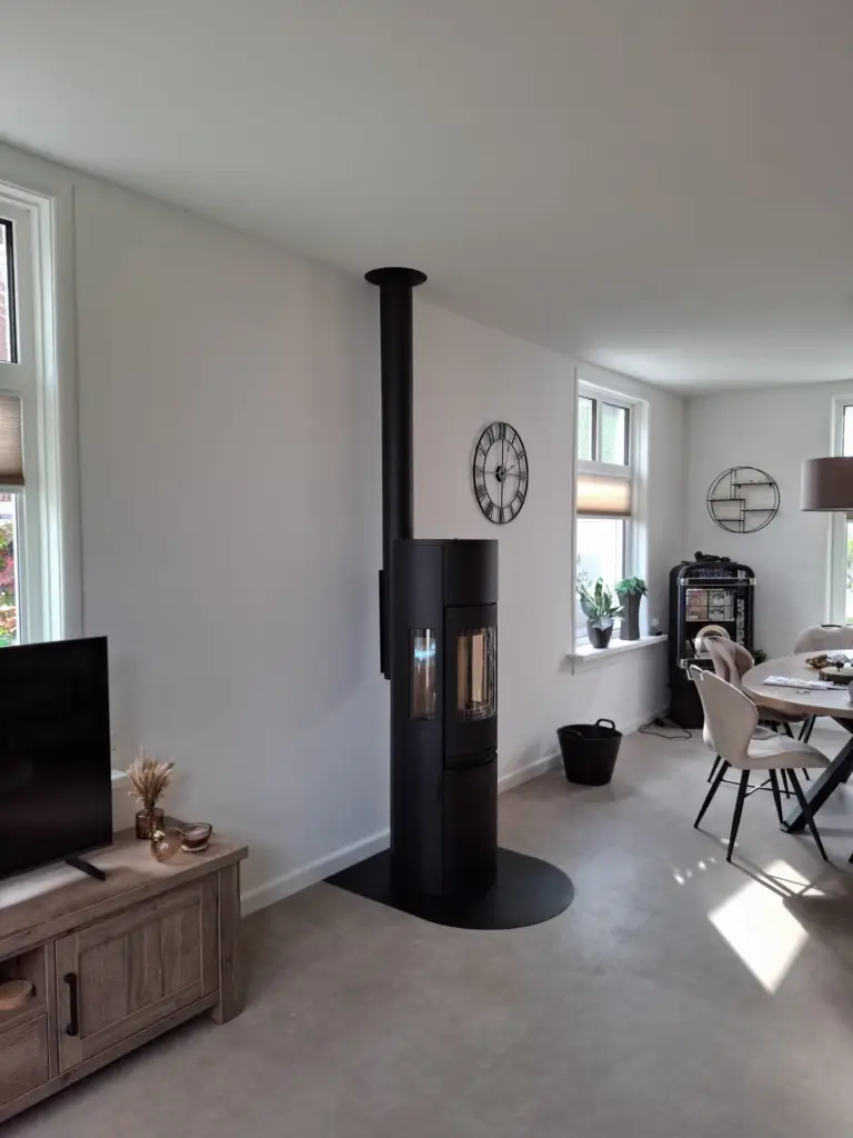 De zwarte Contura 596 Style houtkachel brandt in een woonkamer; houtblokken liggen in de haard en in een mand ernaast.