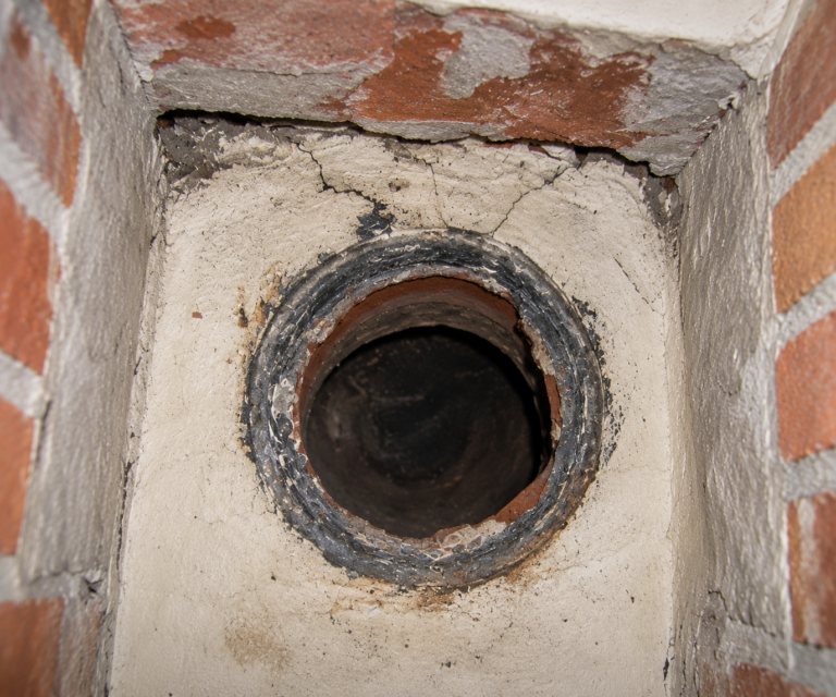 Moderne houtkachel aangesloten op een bestaande gemetselde schoorsteen in een lichte woonkamer.